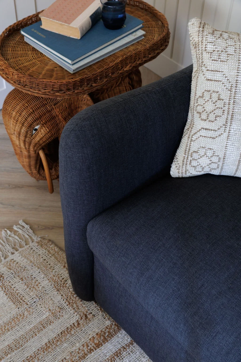 Sofa arm detail with showing rug, pillow and elephant wicker side table.