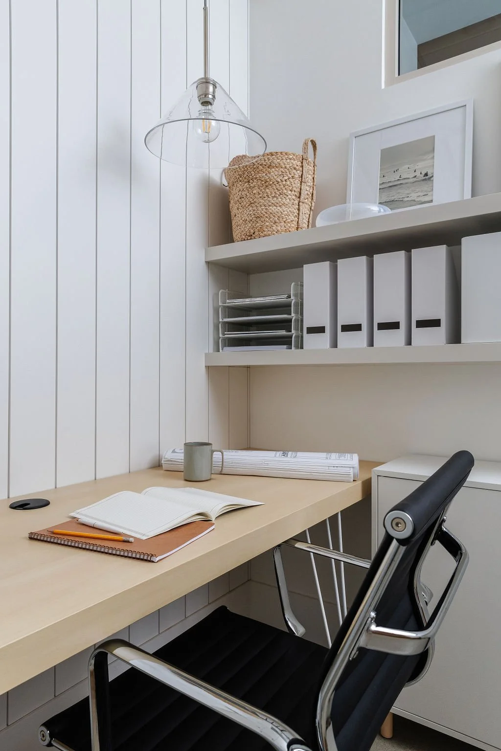 Close-up photo of office desk, black leather office chair and decor on floating shelving. 