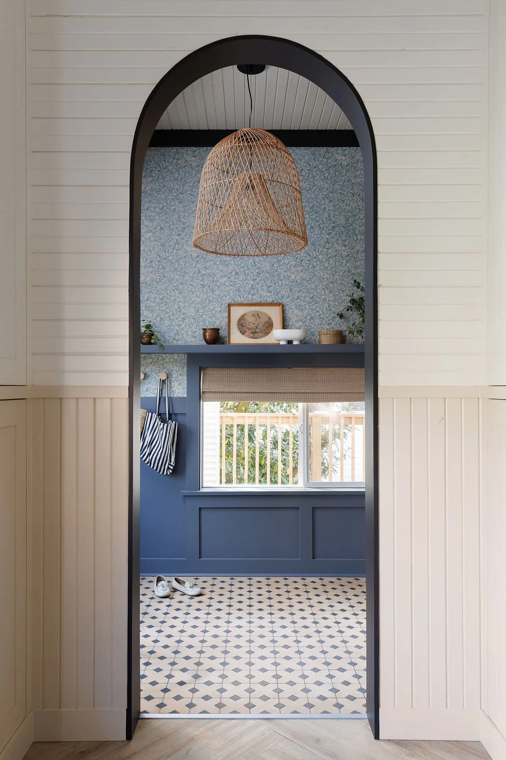 Looking through tall arched door opening to entry with floral wallpaper mosaic tiles and window.
