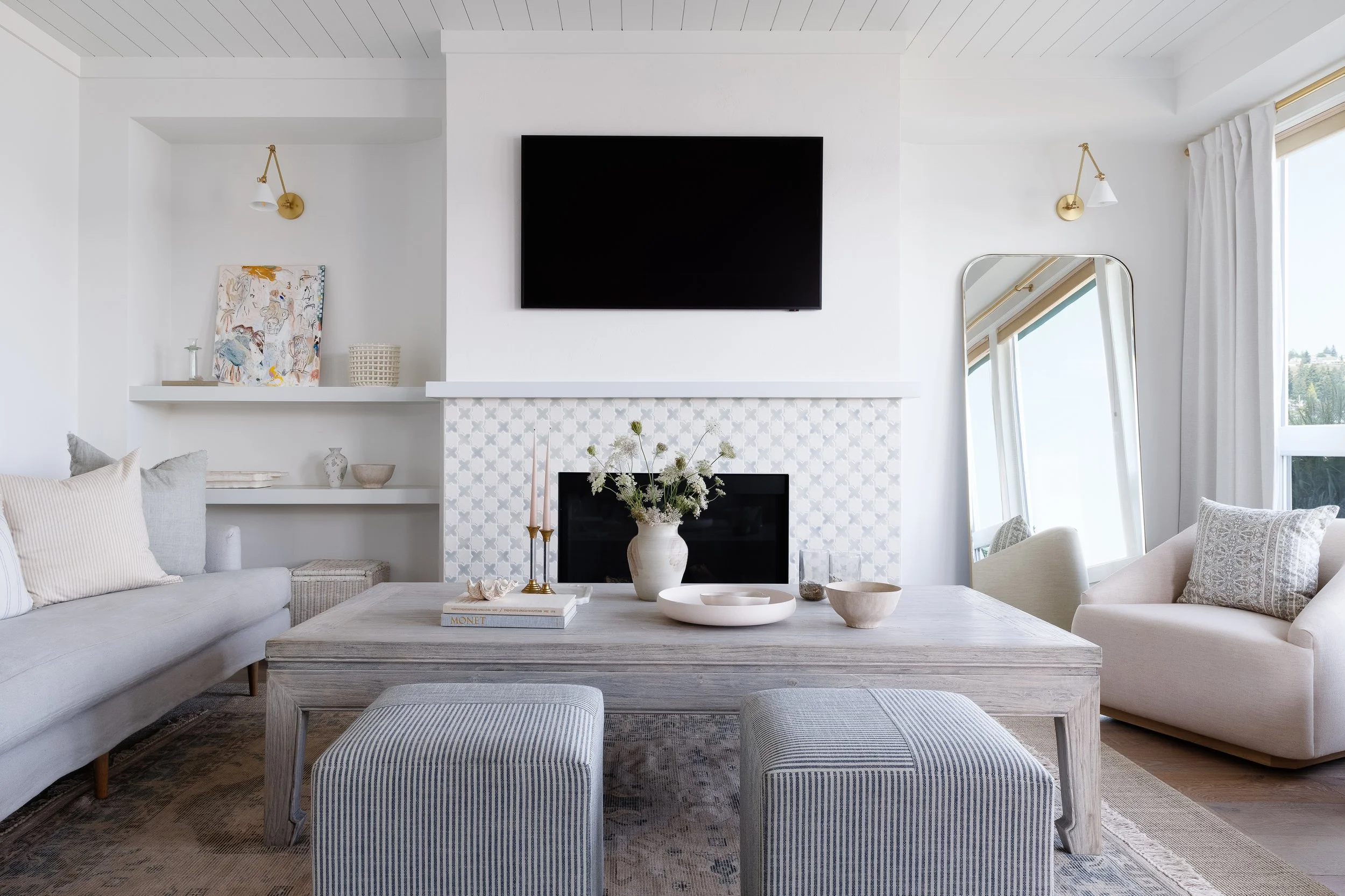 Beach house living room with mosaic tile fireplace, shelving with decor and art, armchairs next to the ocean view and comfortable sofa.