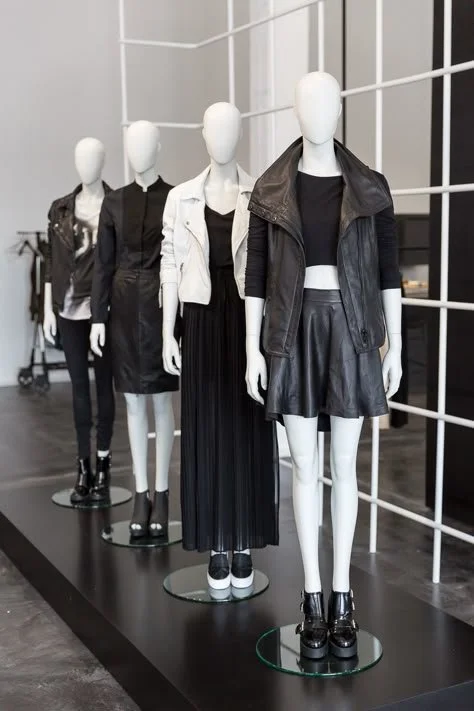 Four mannequins dressed in black and white fashionable clothing, displayed on a black platform inside a clothing store.
