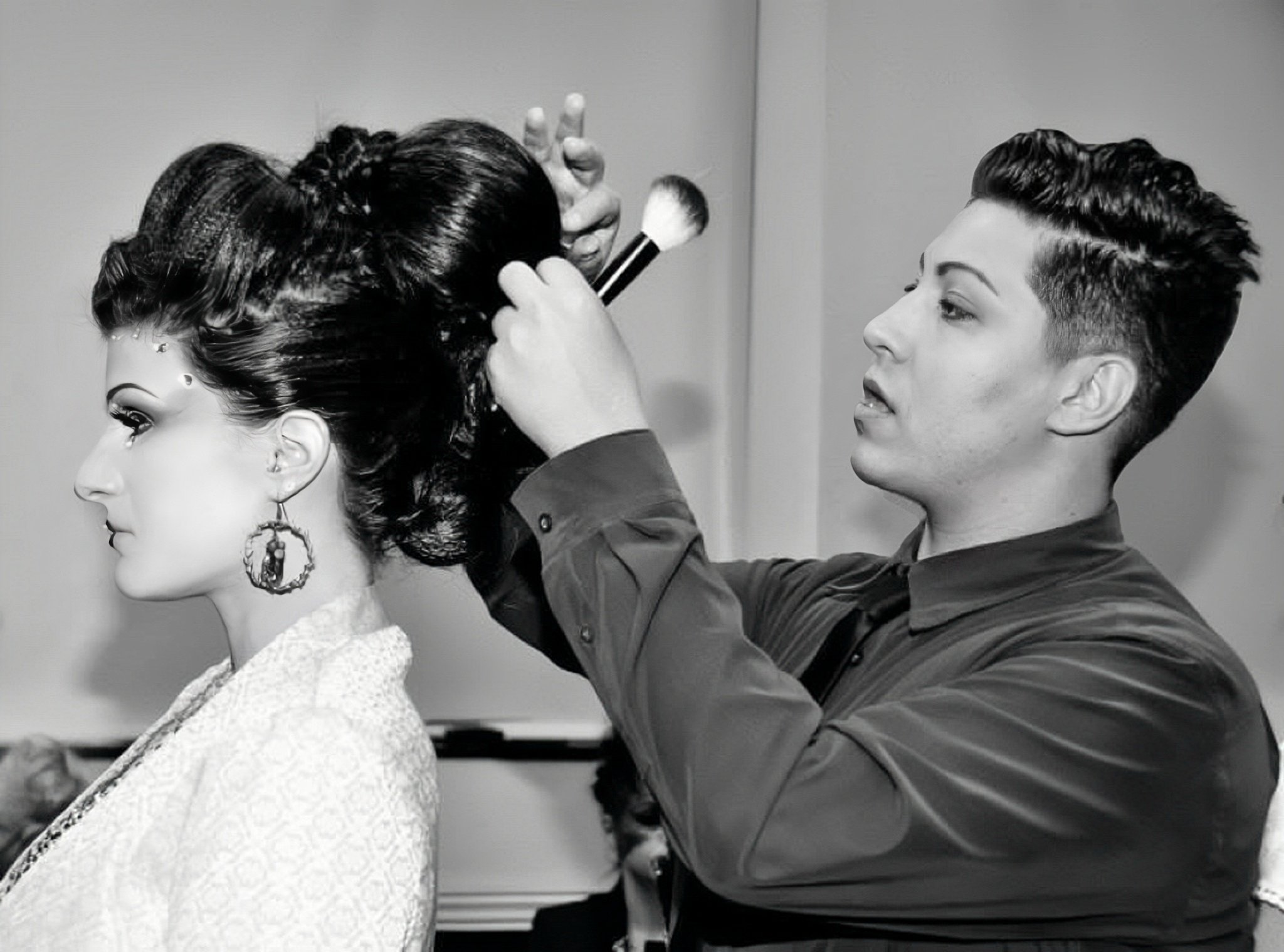 A hairstylist blow-drying a woman’s elaborate updo at a hair show or event.