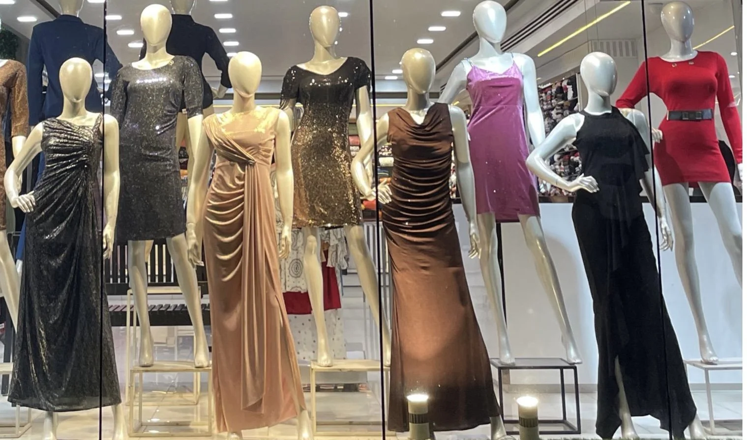 Display of various mannequins dressed in elegant evening gowns and dresses, in a retail store window.