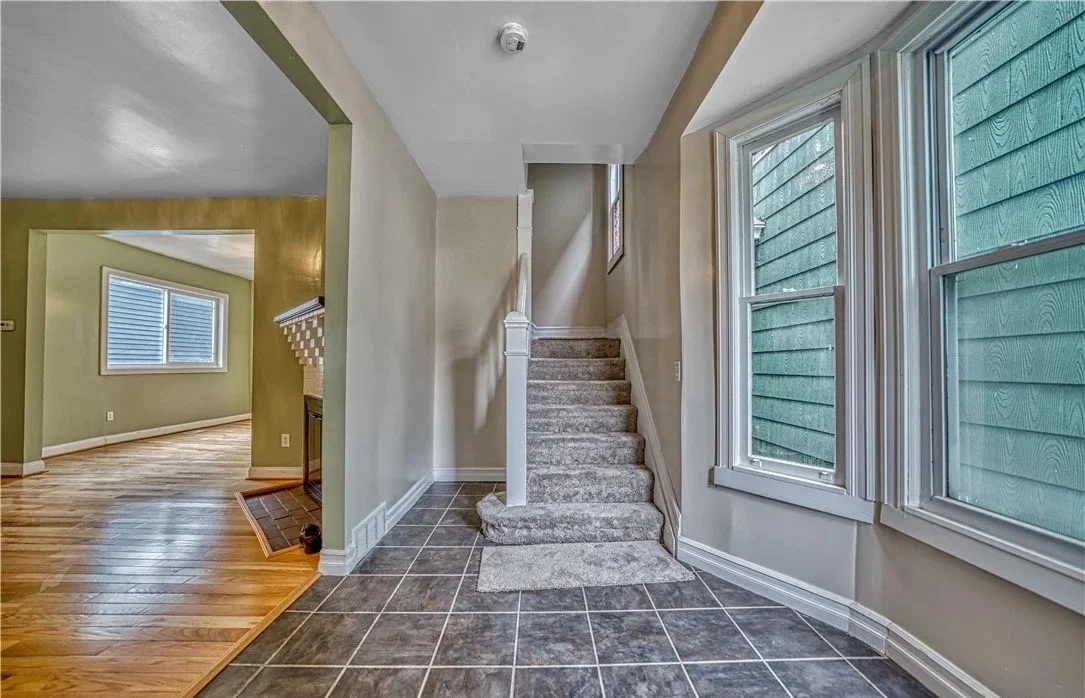Entryway with staircase, tiled floor, and multiple windows, leading into a room with hardwood flooring
