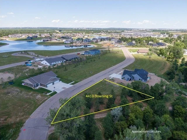 Aerial view of a suburban neighborhood with a pond, houses, and undeveloped lot with yellow lines marking the lot boundaries at 4413 Downing Street.