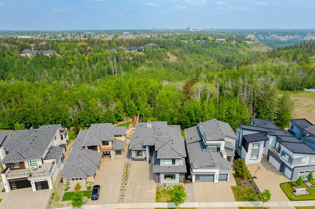 Aerial view of residential homes in a suburban neighborhood with a forested area and rolling hills in the background.