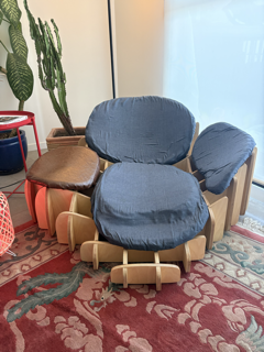 A blue cushioned chair with wooden armrests and a matching footstool, placed on a patterned area rug near a window, with potted plants nearby.
