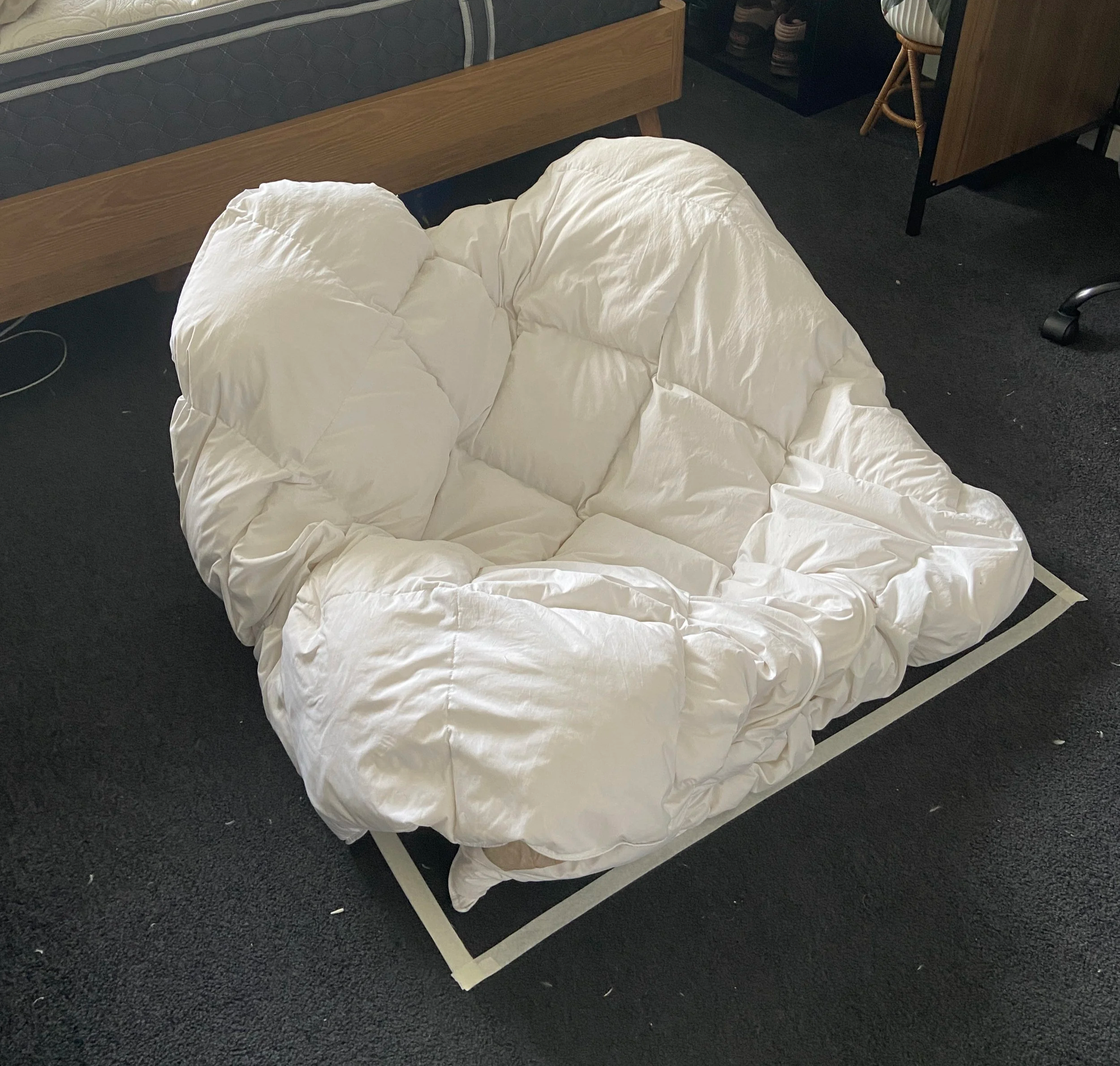 A white, puffy, cushioned lounge chair or bean bag chair on a black carpeted floor in a room with furniture and decor.