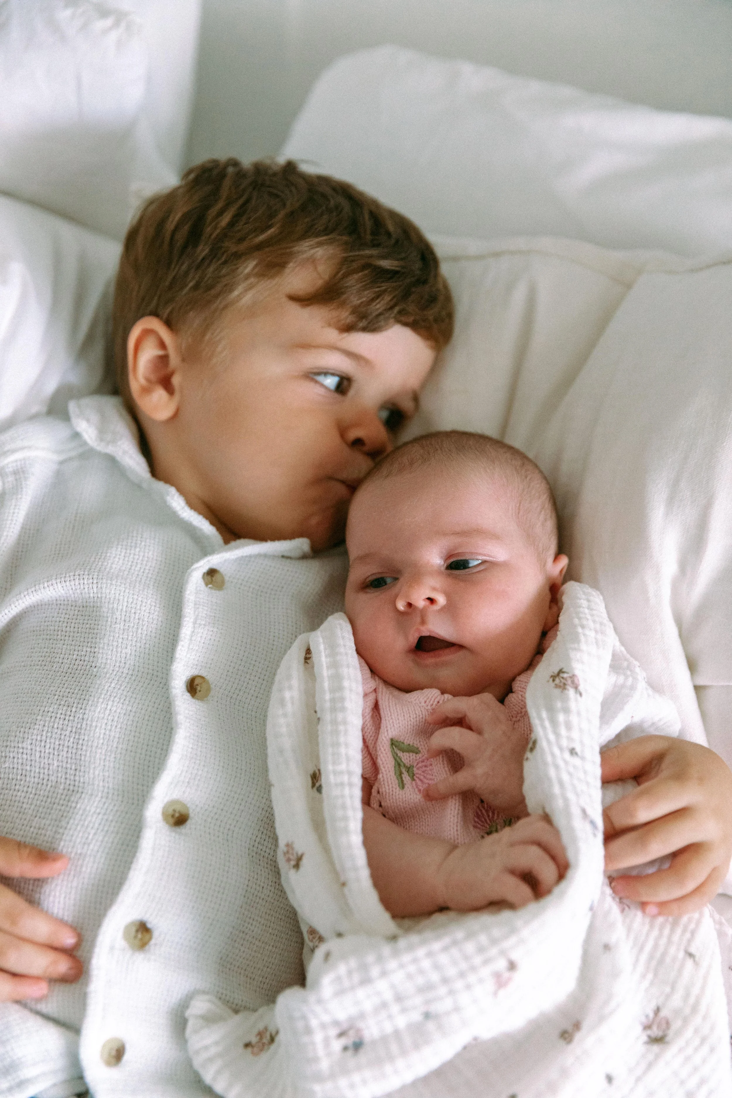 A young boy and a baby lying on a bed, the boy is kissing the baby's forehead.