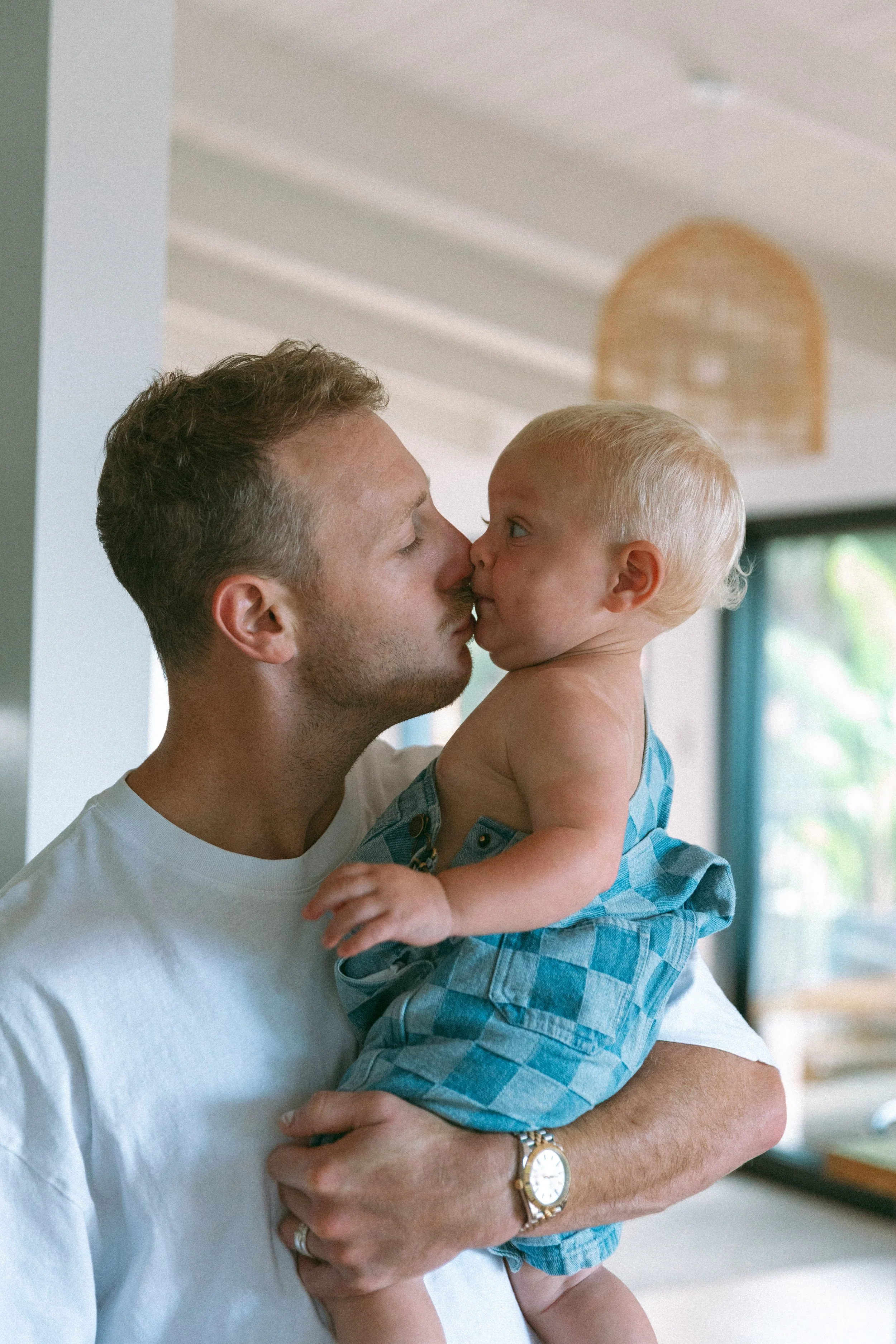 A man holding a toddler boy; they are touching noses and about to kiss.