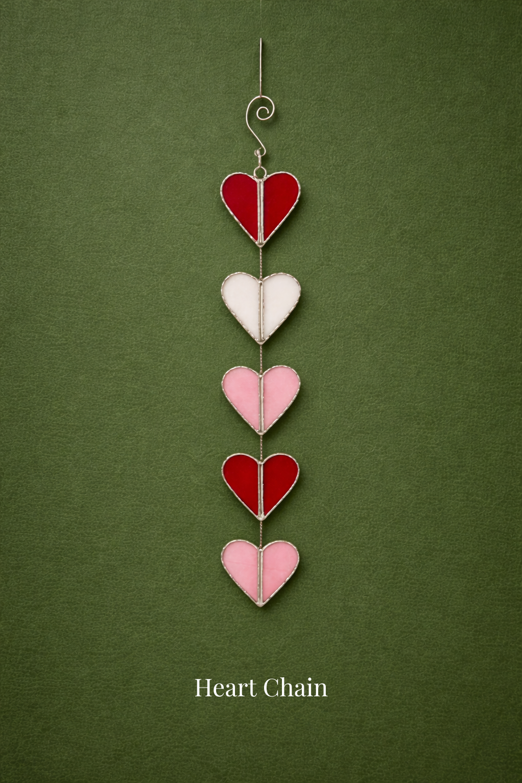 A vertical string of five stained glass hearts in red, white, and pink colors hanging on a metal chain against a green background. The text 'Heart Chain' is at the bottom.