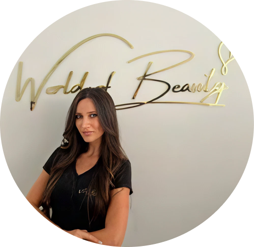 A woman standing in front of a wall with gold cursive lettering that says "Waldorf Beauty."