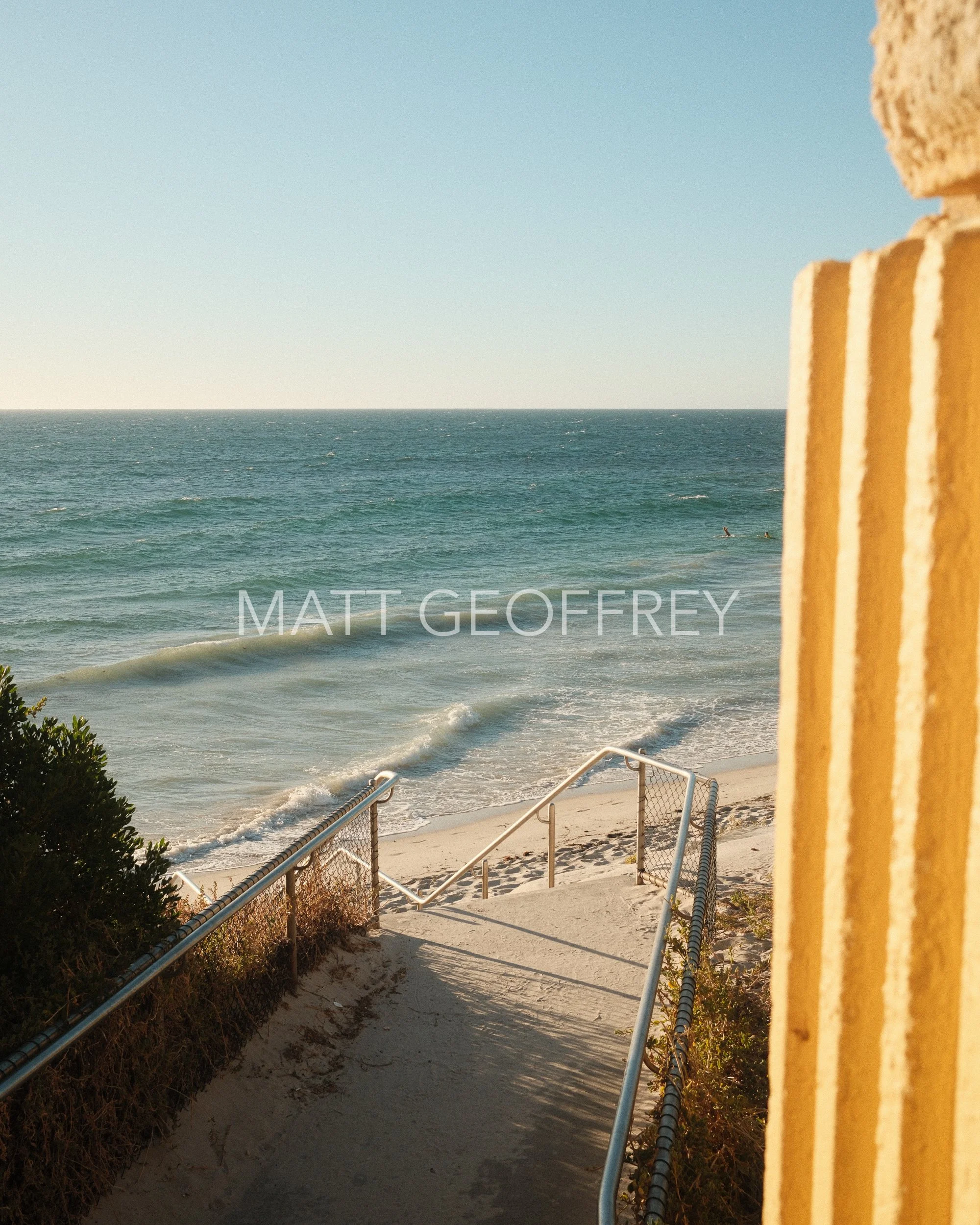 A view of a staircase leading down to the beach, with the waves crashing by the shore of yellow sand
