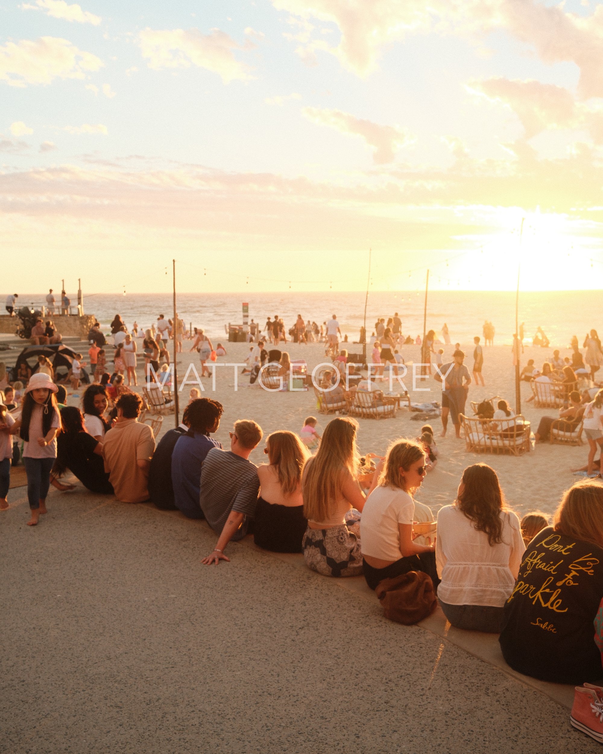 People sitting on the beach, looking out at the ocean where the sun is setting