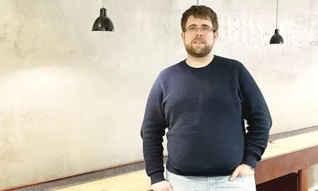 En mann står foran en hvit vegg med to hengende lamper over ham.