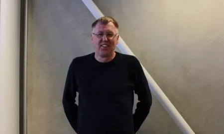 En mann står foran en vegg med en kabel eller stang som heller.