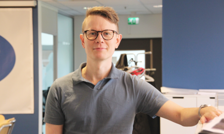 Person med briller står i et moderne kontormiljø.