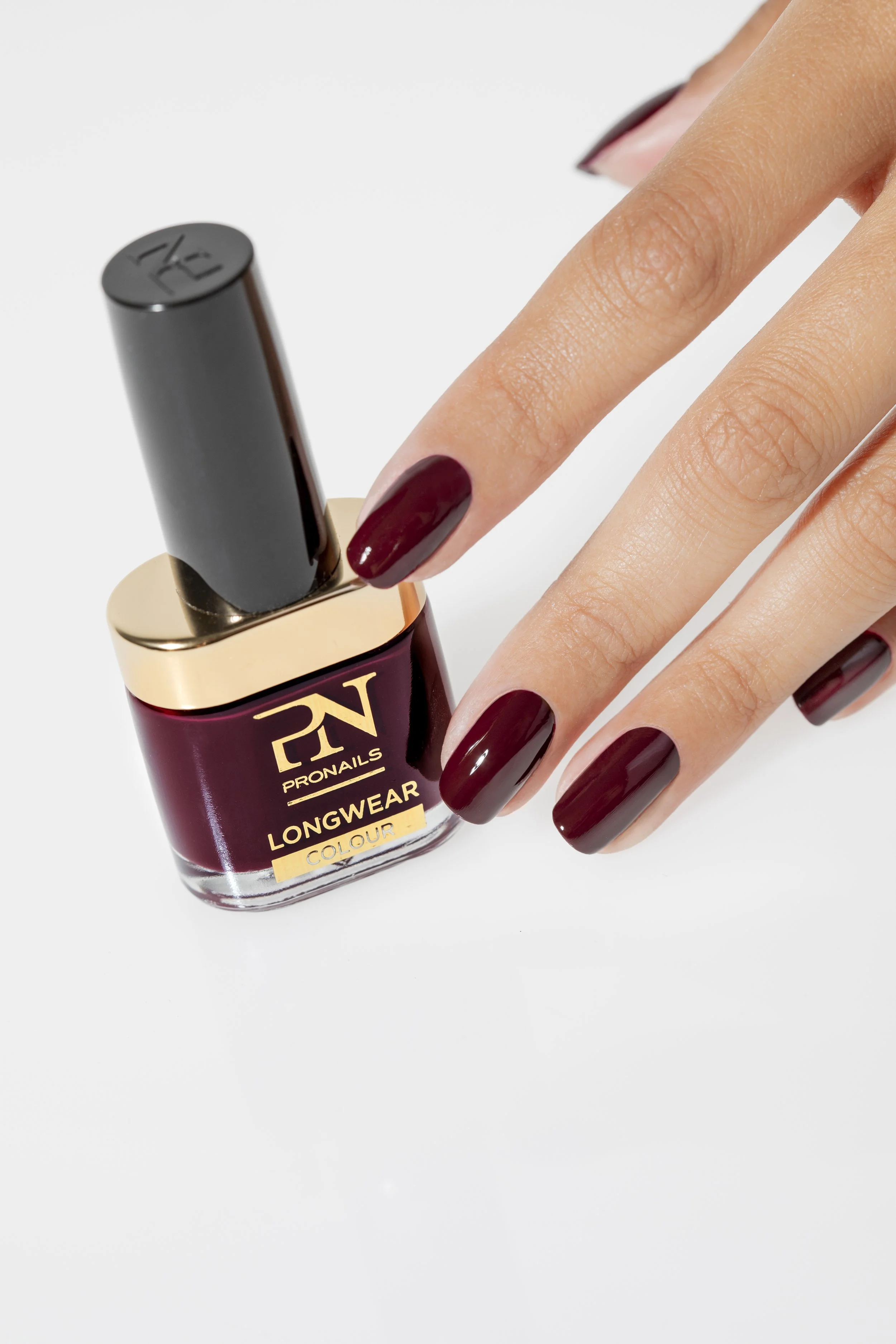 Hand met nagellak in een donkerrode kleur naast een fles nagellak van PRONAILS LONGWEAR.