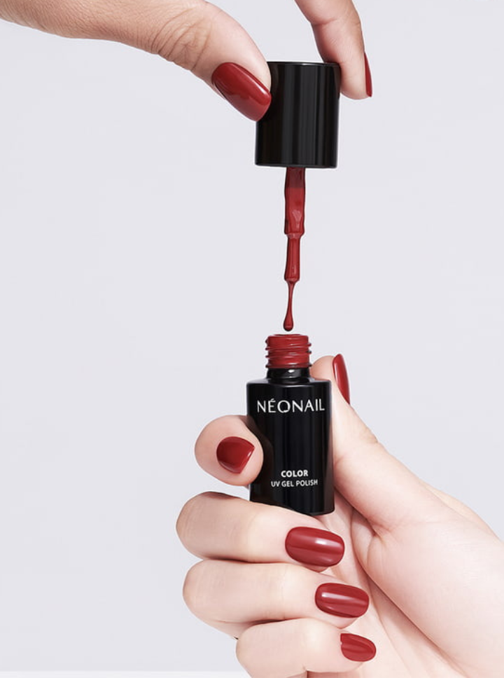 Twee handen, één met rood lakje, houden een flesje nagellak vast en een penseel die uit het flesje komt, met een witte achtergrond.