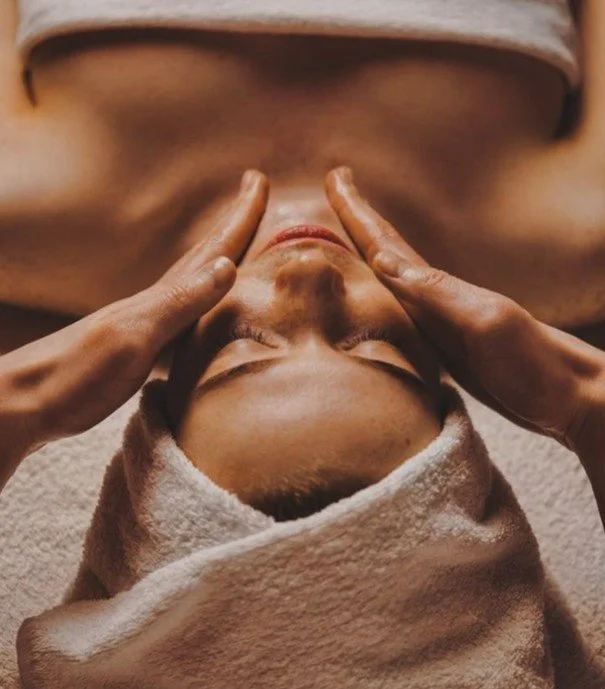 Persoon krijgt een gezichtsmassage in een spa of wellnesscentrum, met een handdoek om en handen die het gezicht masseren.