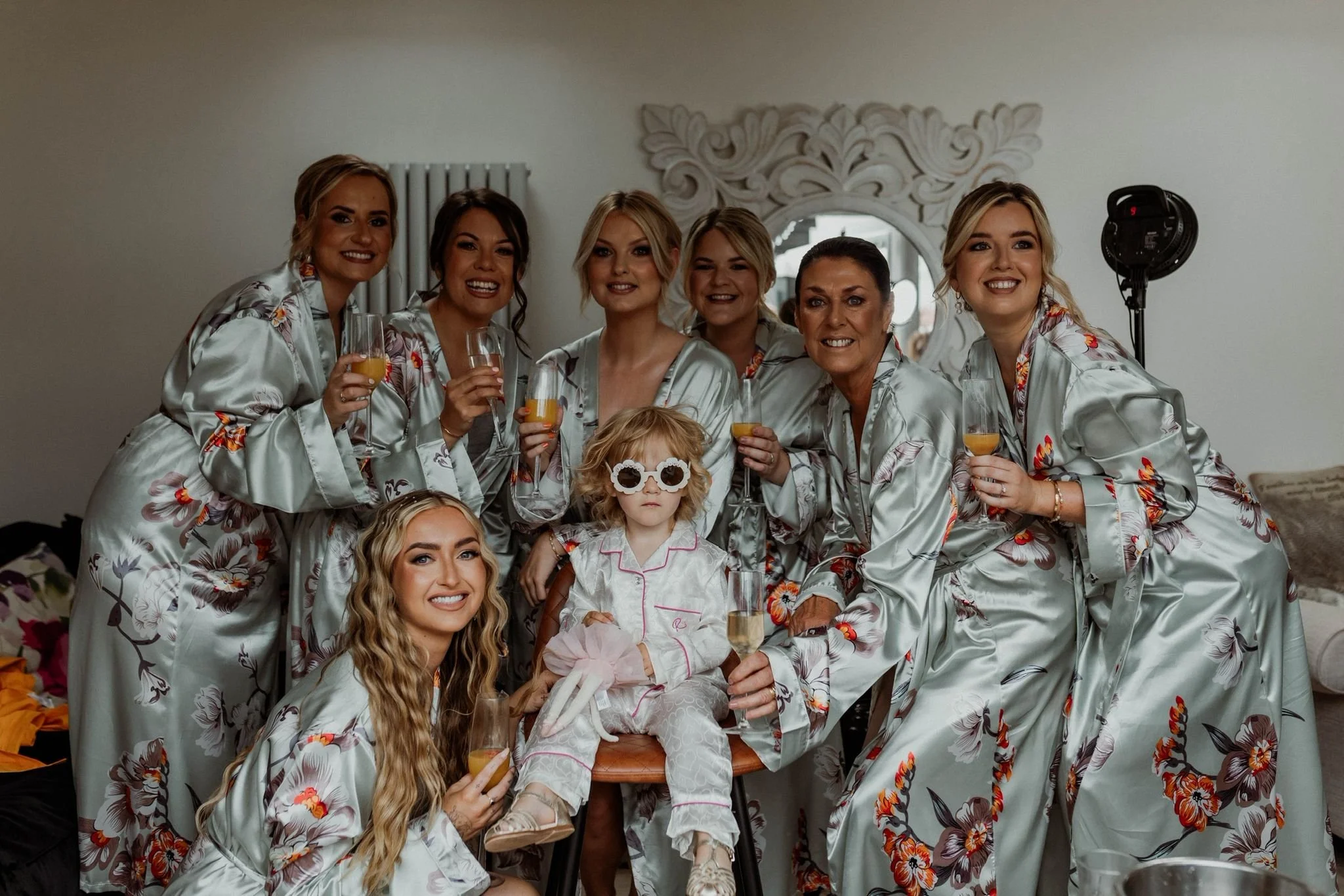 A group of women and a young girl in robes, celebrating with drinks in a room, smiling at the camera.