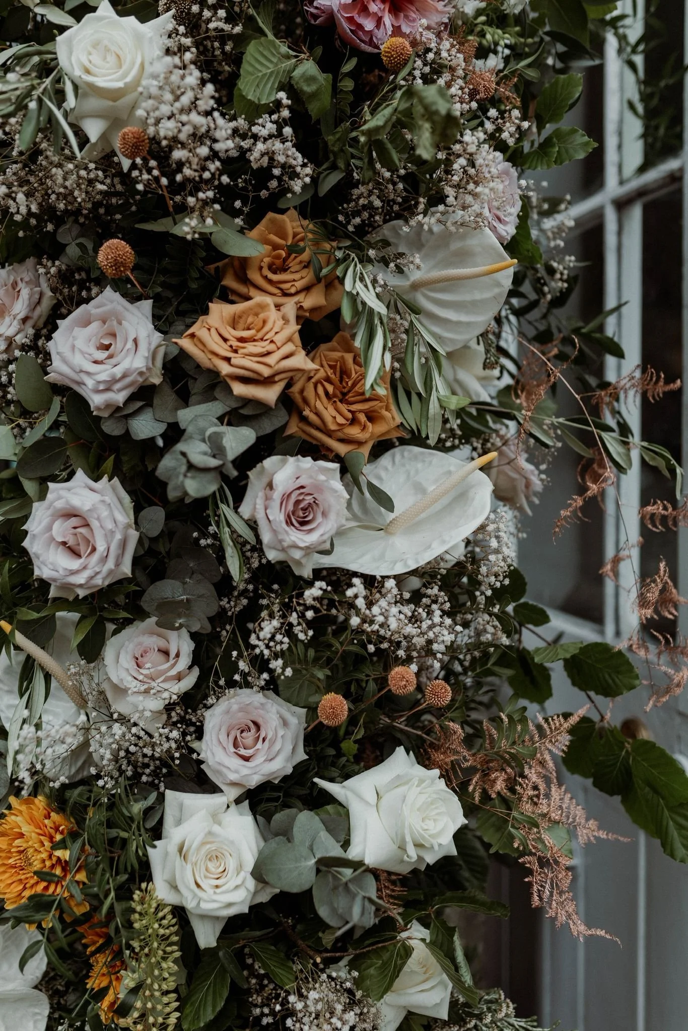 A vertical arrangement of mixed flowers including roses, calla lilies, baby's breath, and greenery.