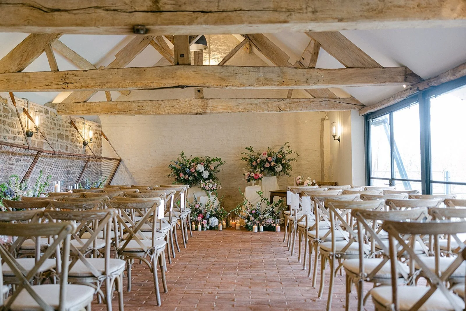 Wedding ceremony setup with chairs facing an altar decorated with pink and white flowers and candles in a rustic venue with exposed brick and wooden beams.