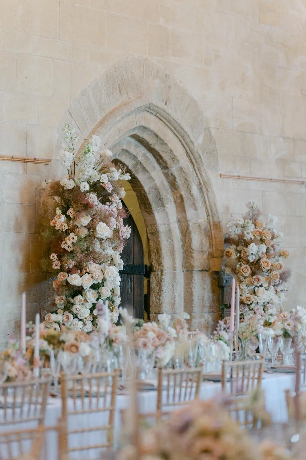 Elegant event table setup with floral arrangements and a stone arched doorway in the background.