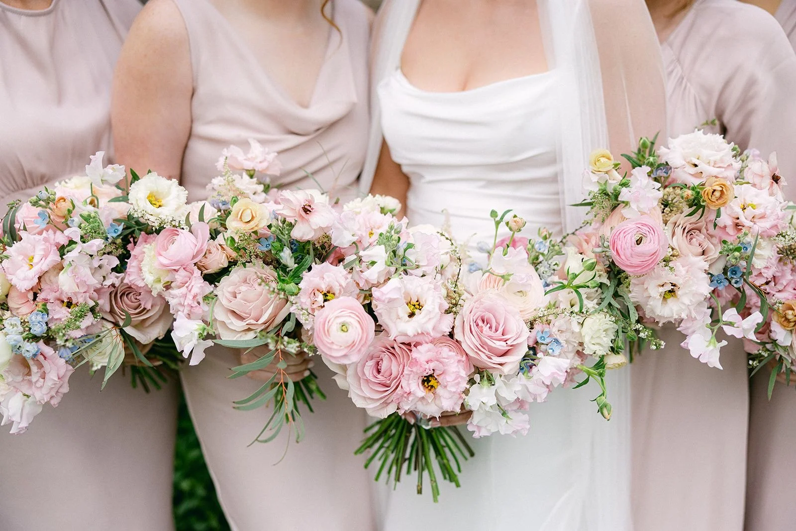 A bride and her bridesmaids holding pink and white floral bouquets at a wedding.