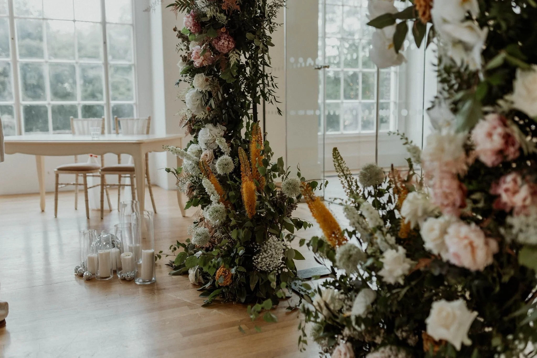 A floral arrangement with white, pink, and orange flowers, and greenery in a decorated indoor space with large windows.