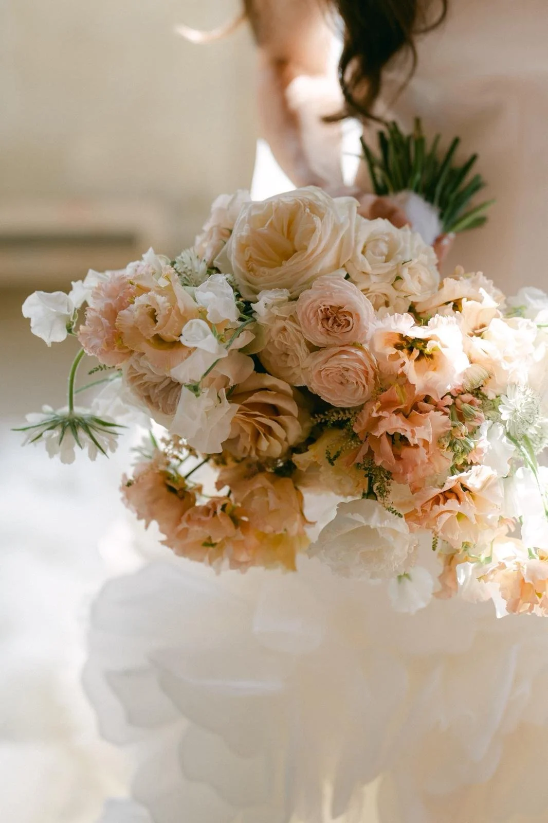 Close-up of a wedding bouquet with cream, blush, and peach-colored roses and other flowers.