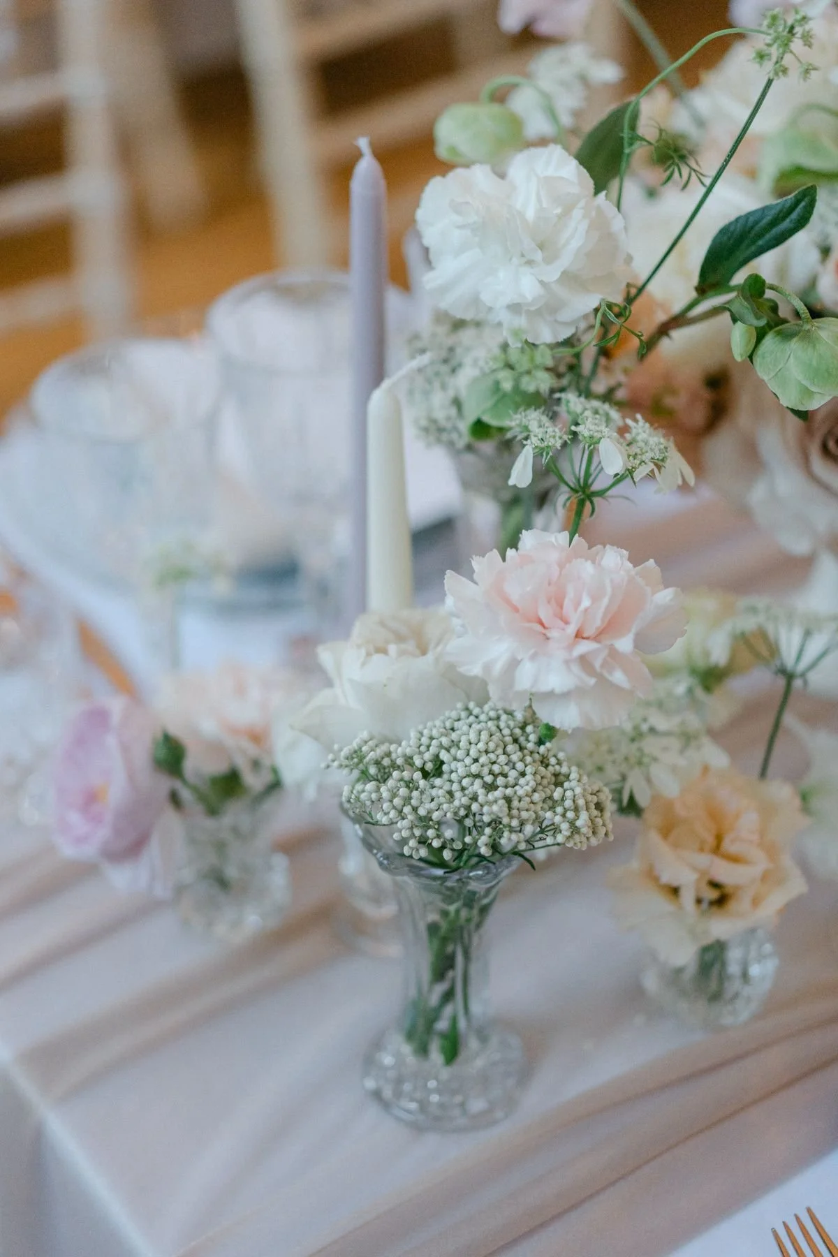 Elegant floral centerpiece with white and blush pink flowers in glass vases on a table with white tablecloth at an event.