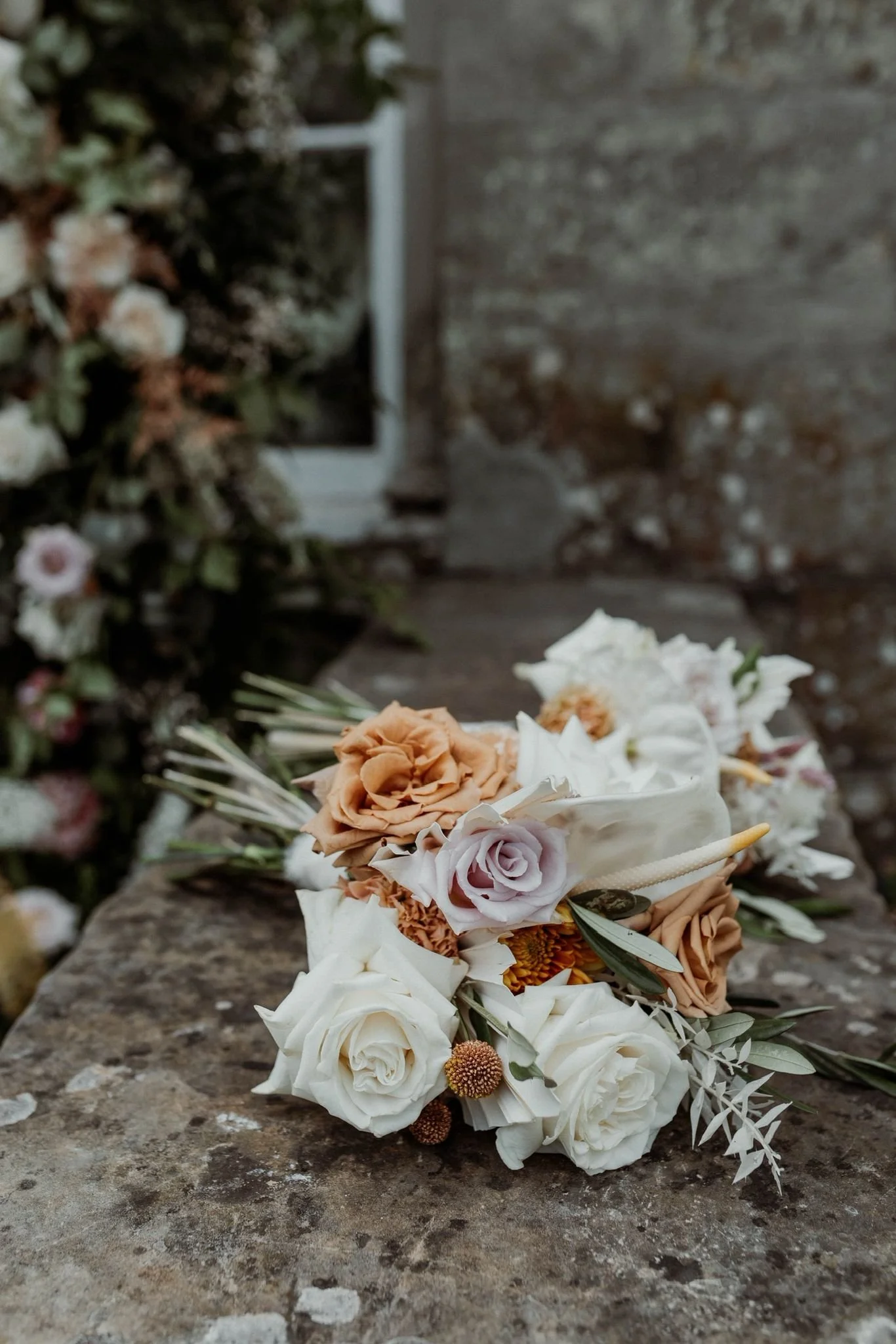 A bouquet of white, peach, and pink roses with greenery, placed on a weathered stone surface outdoors.