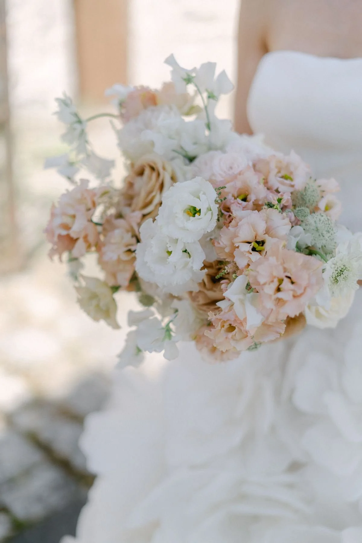 A wedding bouquet with white, blush pink, and cream-colored flowers, held by a bride in a white dress.
