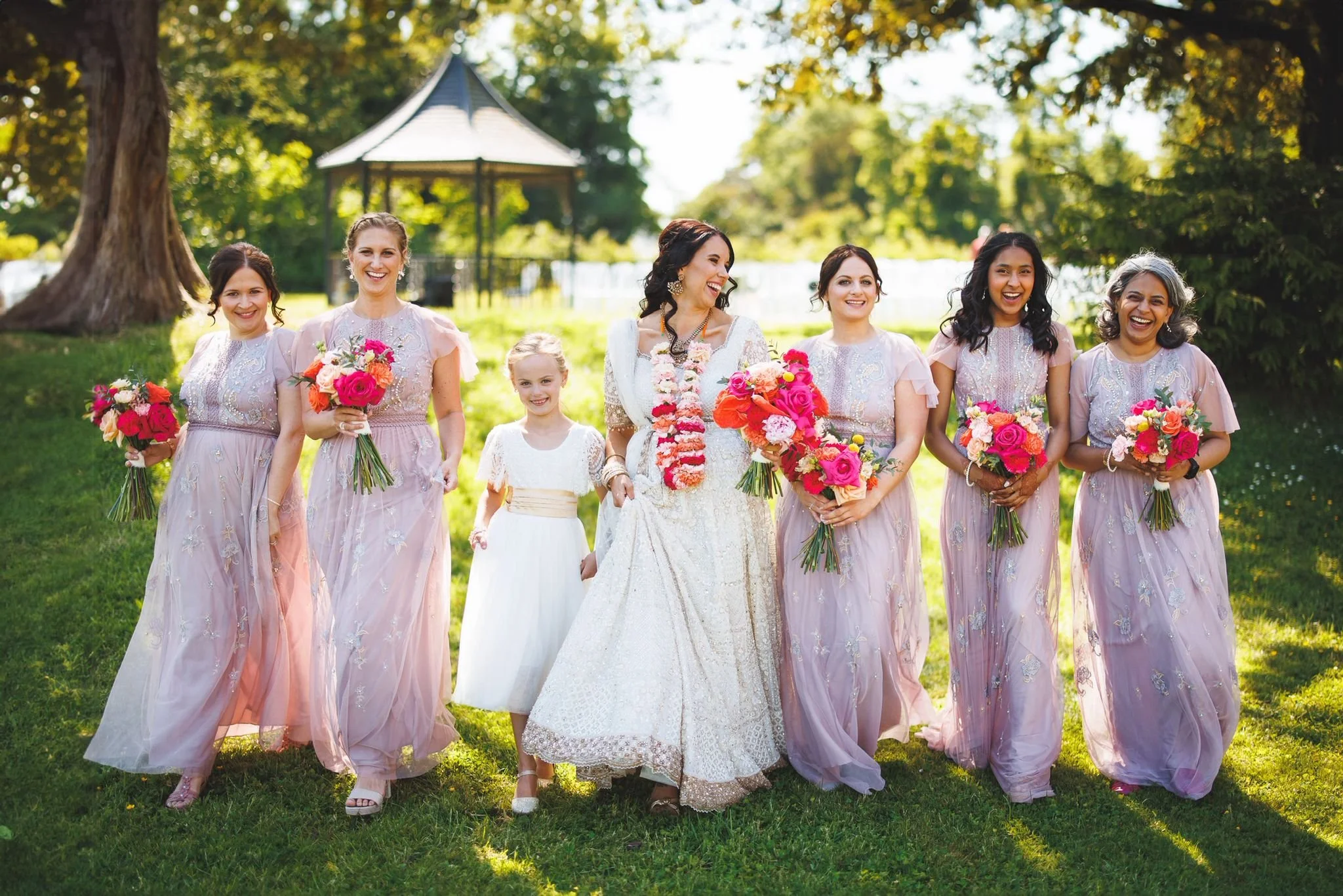 Group of women in pastel dresses holding bouquets, walking outdoors in a park during daytime.