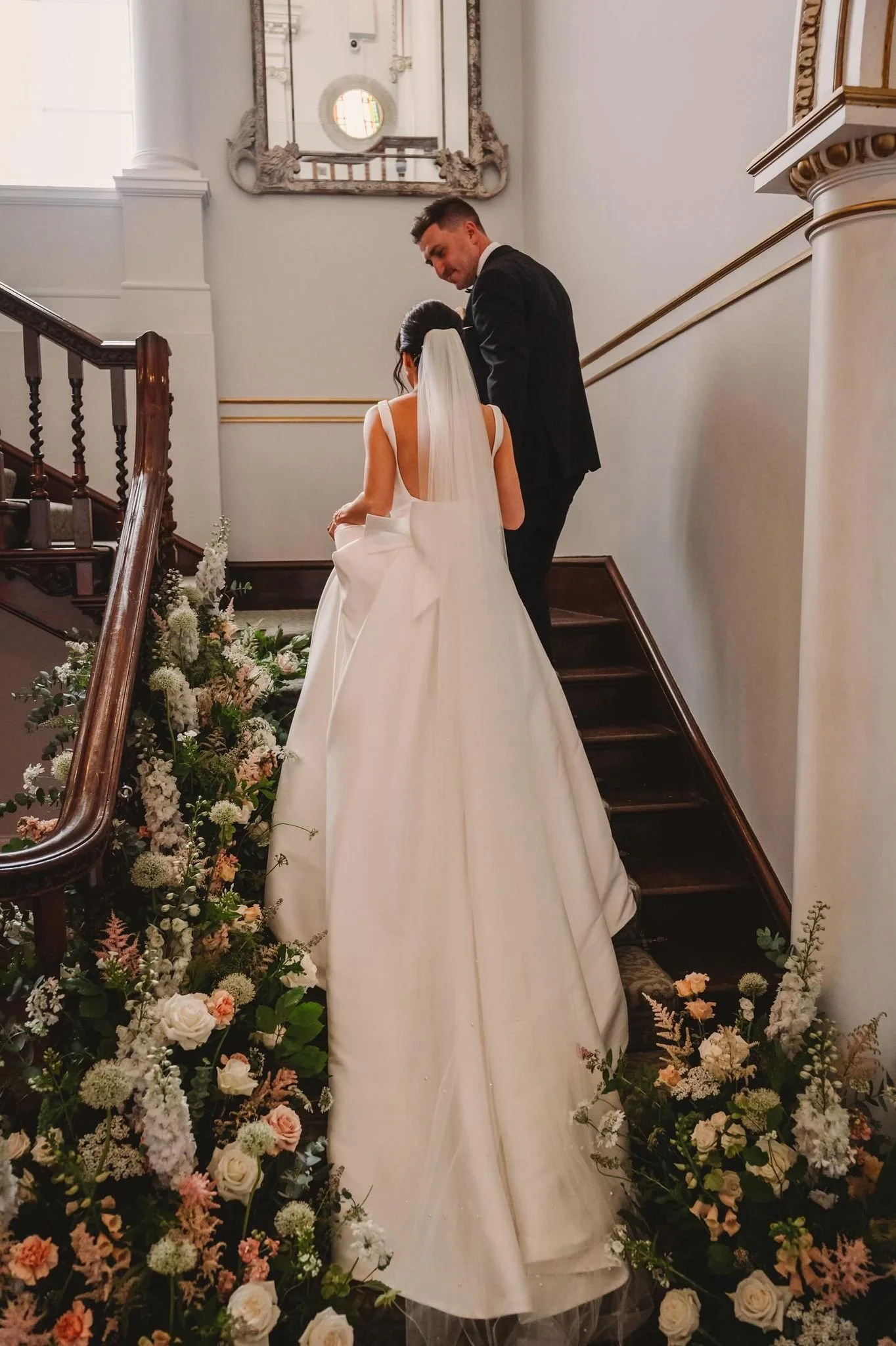 A bride and groom standing on staircase during their wedding ceremony, surrounded by floral decorations.