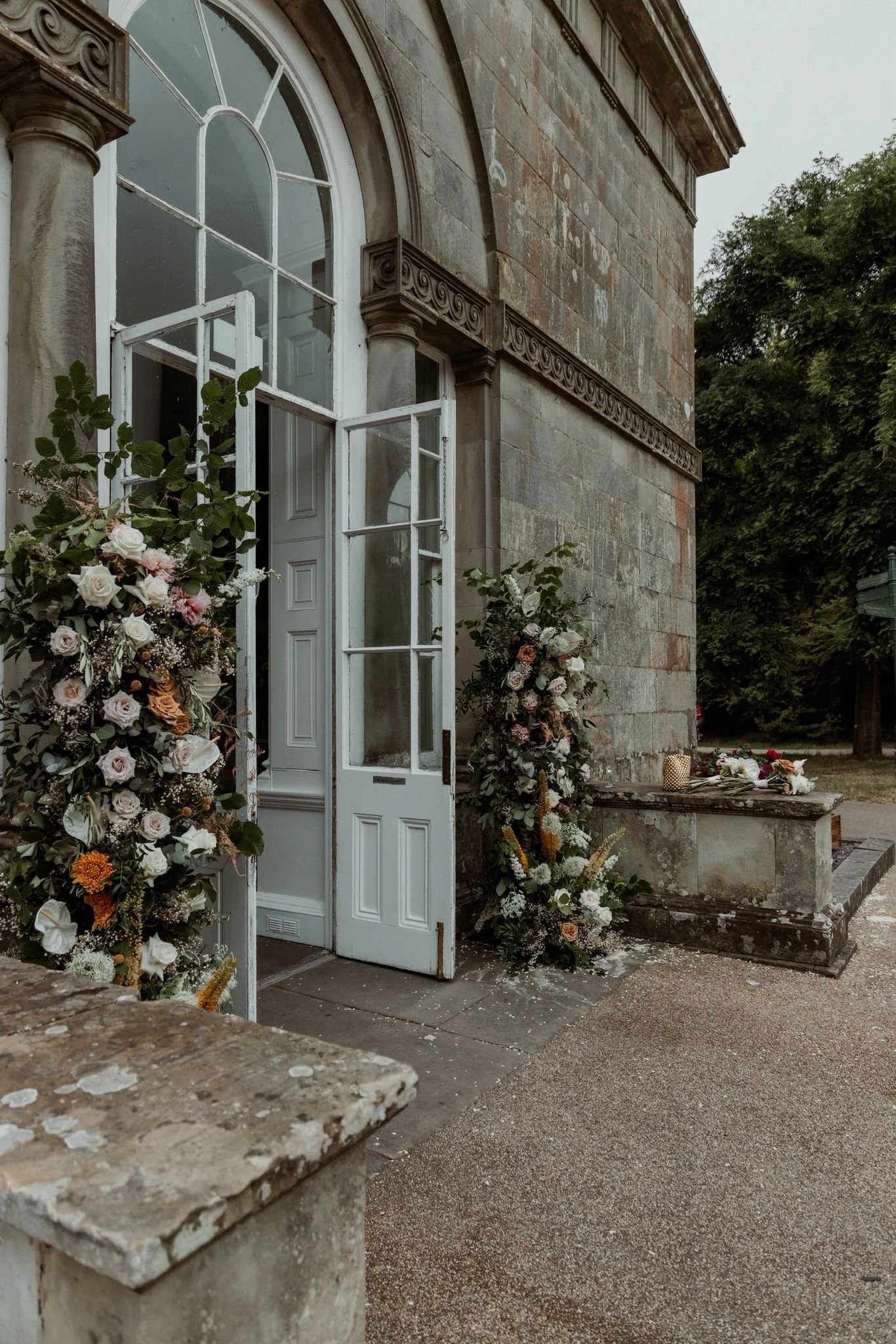 Open white door of a stone building decorated with flowers, with a table holding more flowers and candles outside on a stone ledge.