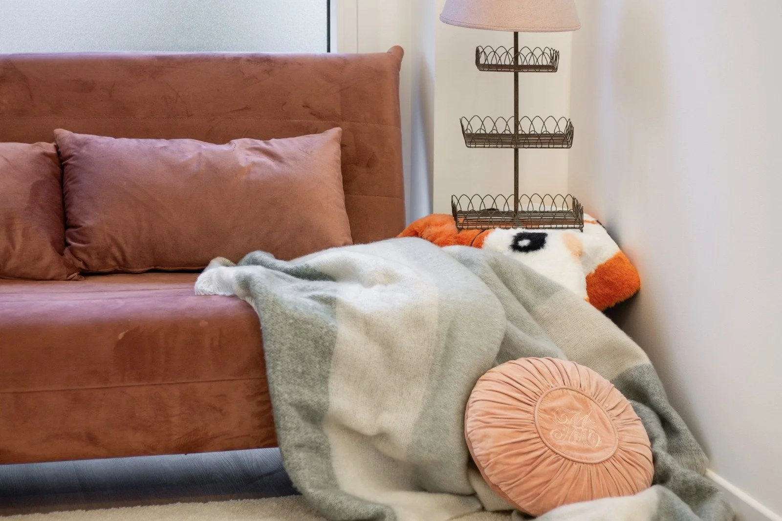 Bright living room with white walls, large window/door leading to balcony, beige sofa with decorative pillows, black floor lamp, patterned white rug, and built-in bookshelf with decor items.