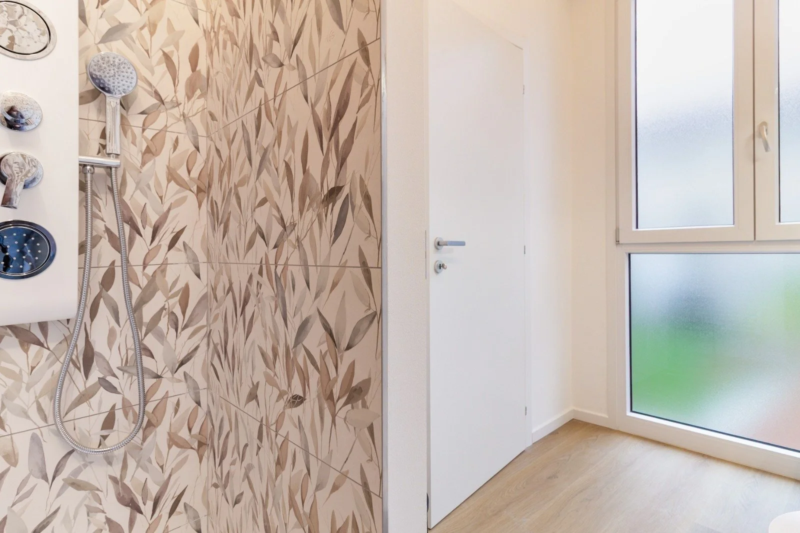 Modern bedroom with a black metal bed frame, beige blanket, pillows, a hanging plant, large windows, and a wooden floor with a rug.