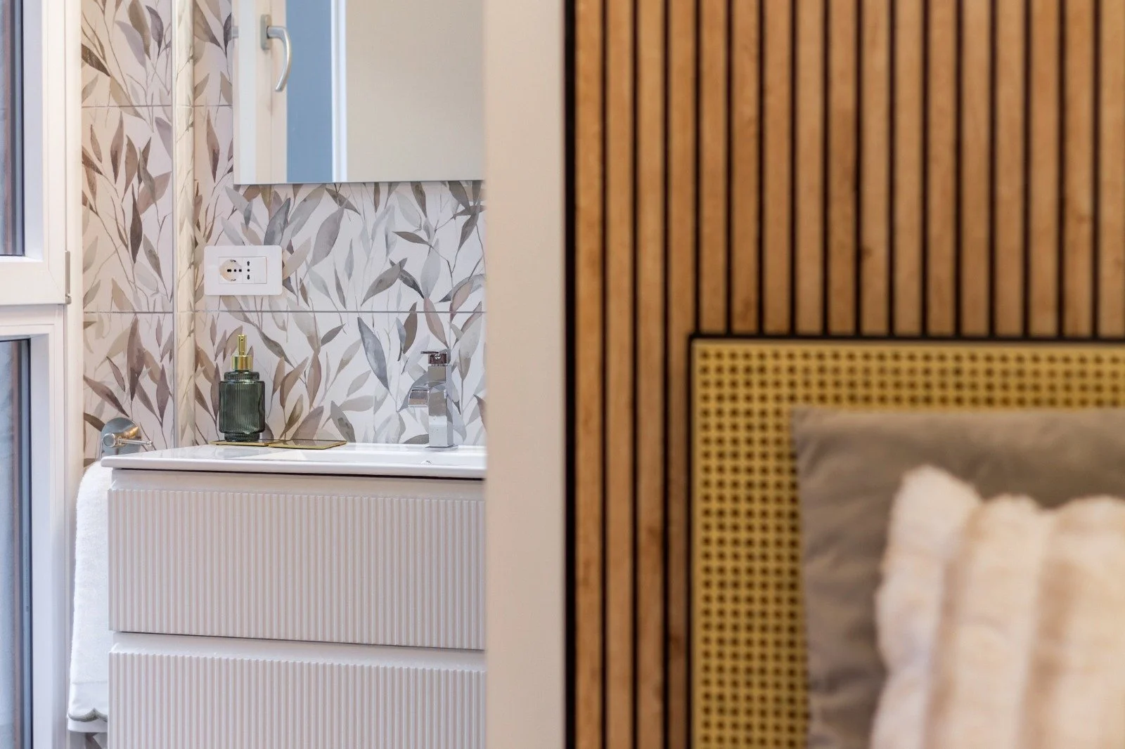 Living room with beige sofa, decorative pillows including one with a woman's portrait, and a wooden shelving unit near a window.