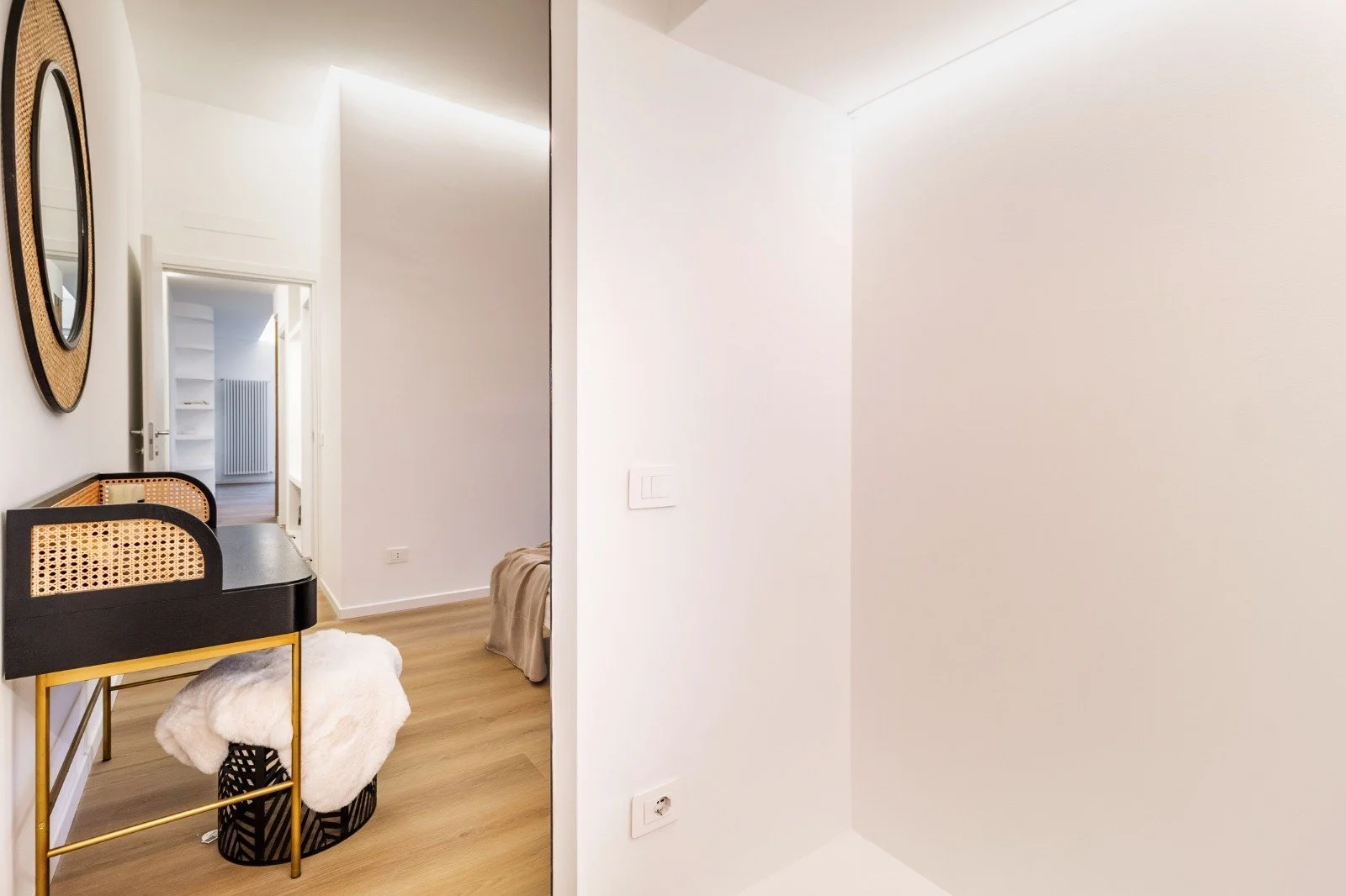 View of a bright, modern bedroom with a balcony, a bed dressed in pink and floral bedding, decorative pictures, a fluffy rug, and wooden flooring.