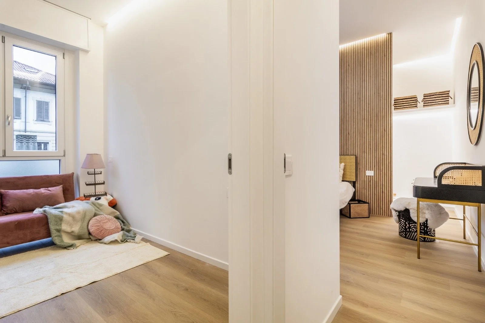A kitchen sink with running water, a glass pitcher, two apples, a wicker basket, and a wooden countertop.