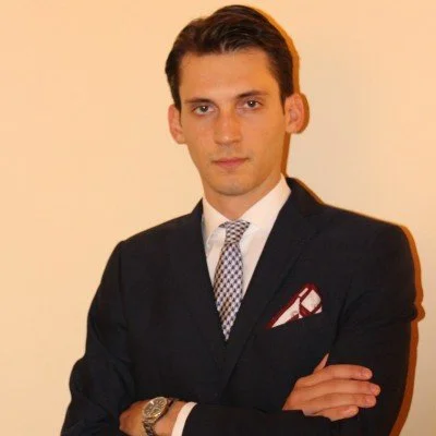 Uomo in giacca elegante con cravatta, braccia incrociate, sfondo neutro.