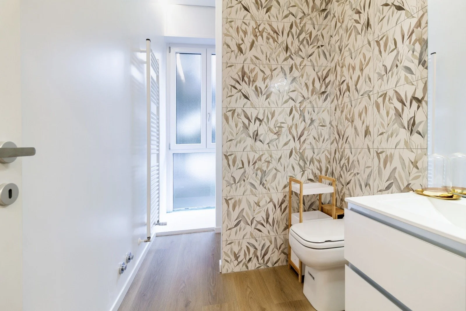 Bright kitchen with white cabinets, wooden countertop, and a dining area with four beige upholstered chairs. Large windows with a view of greenery, and some small decorative items on the counter.