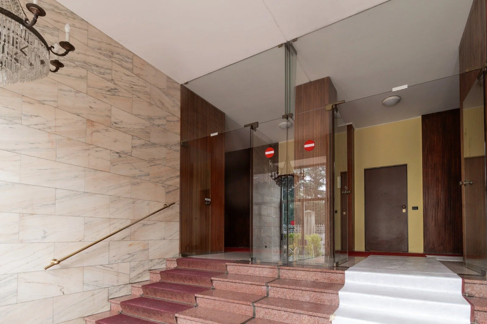 Bedroom with a bed featuring a black metal frame and an arch design, wallpaper with green leaves and palm trees, a window with a hanging plant, a small side table with decor, and a rug on wooden floor.