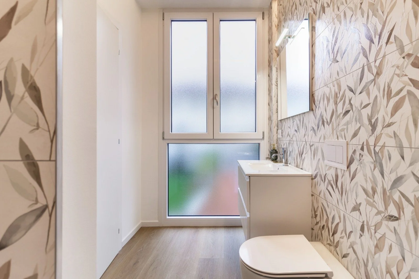 Modern bathroom with a walk-in shower with terrazzo tiles, white walls, a double vanity with green textured cabinets, large mirror, wooden flooring, and a towel hanging from the vanity.
