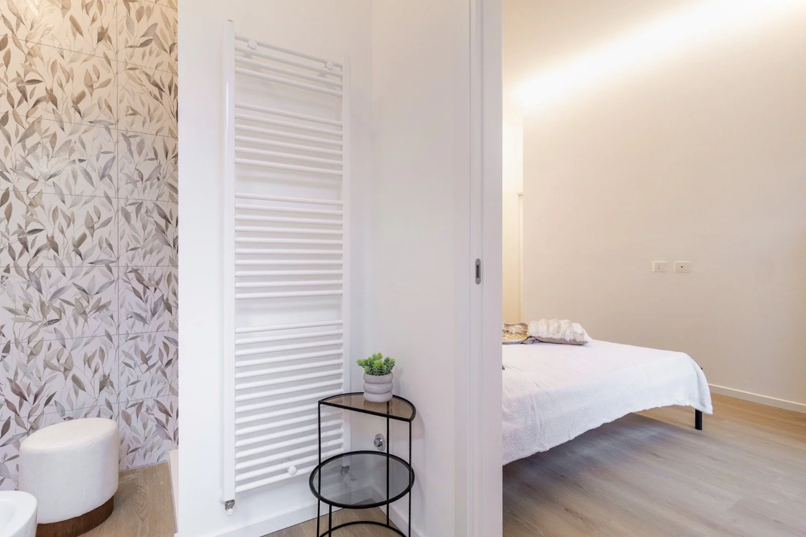 A double sink bathroom vanity with two modern chrome faucets, one with water running and one off, a rolled-up white towel draped over the edge, and a floral-patterned container with a gold lid on the counter.