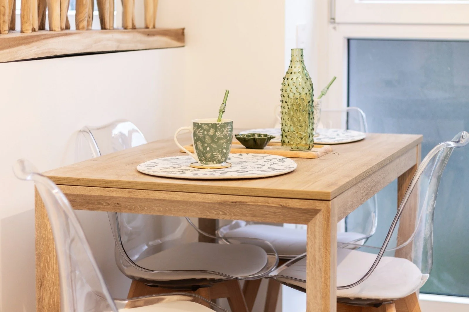 Bright living room with white walls, a black pendant lamp, a beige sofa with dark and colorful pillows, a white rug, and an open kitchen with a dining area and light wooden flooring.