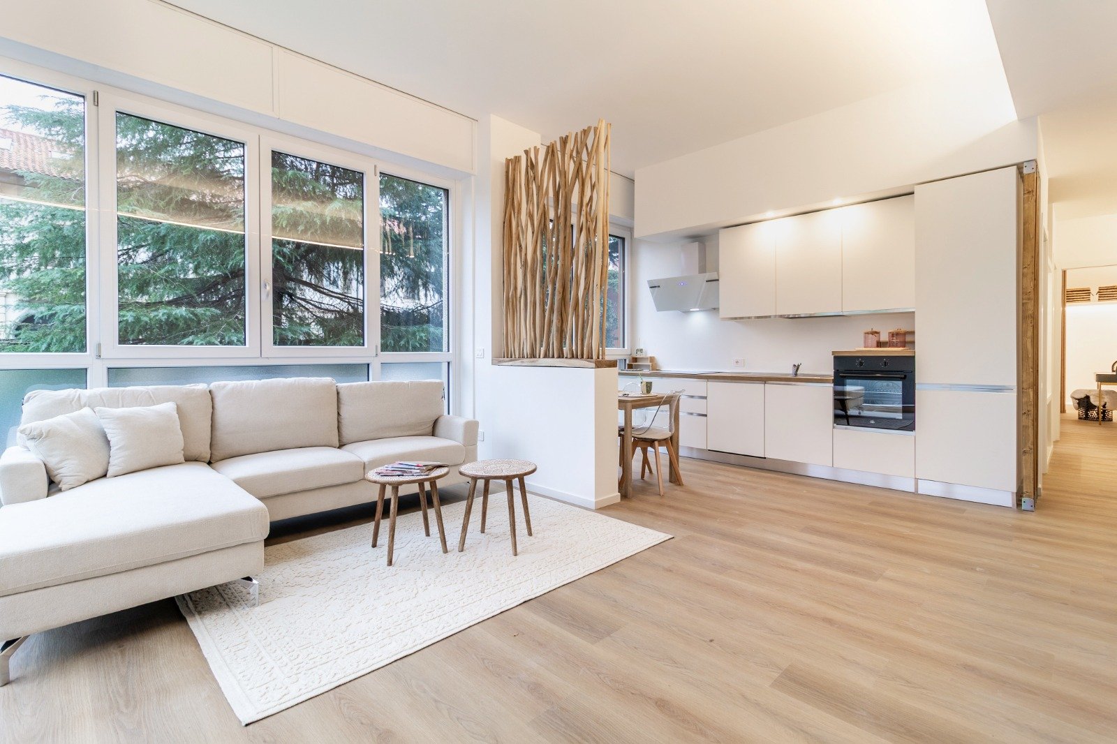 Bright living room with sofa, decorative pillows, large window, and a balcony with outdoor seating and greenery.