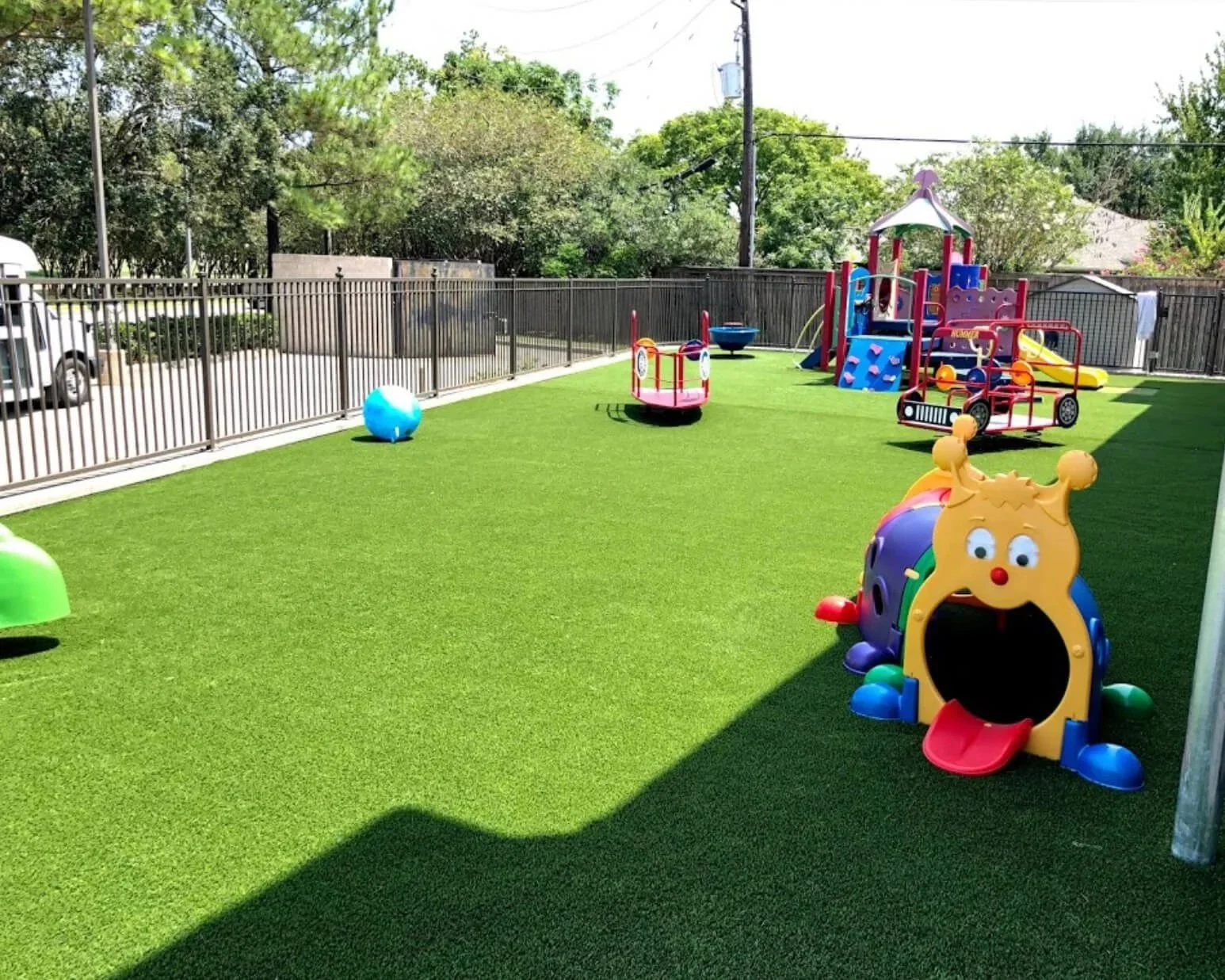 Colorful playground area with slides, climbing structures, and a bounce house in a fenced outdoor space with artificial grass.